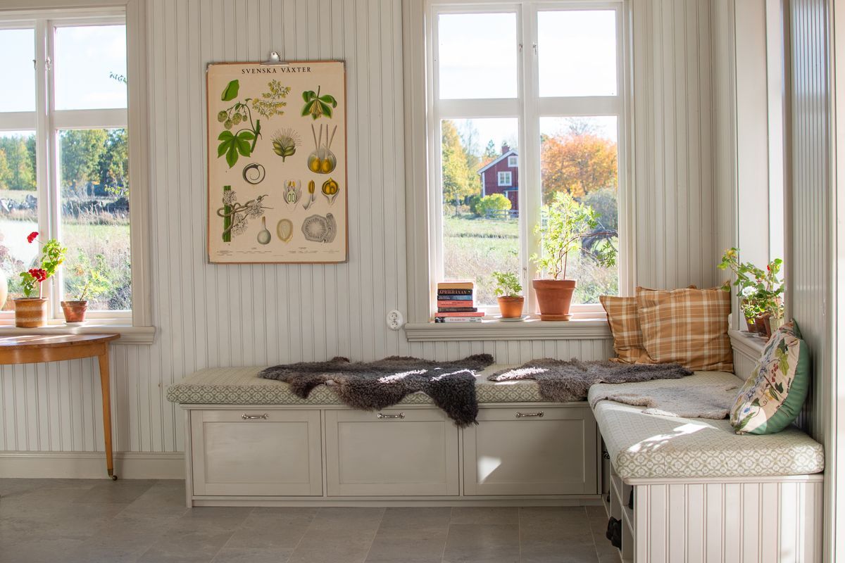 Ljust rum med fönster, bänk och affisch på väggen.