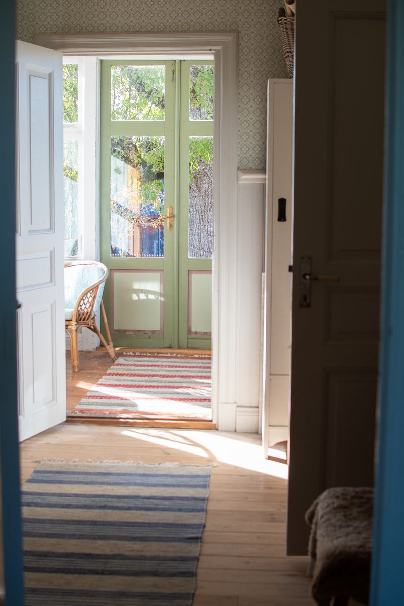 Ljust rum med solbelyst golv och grön dörr.