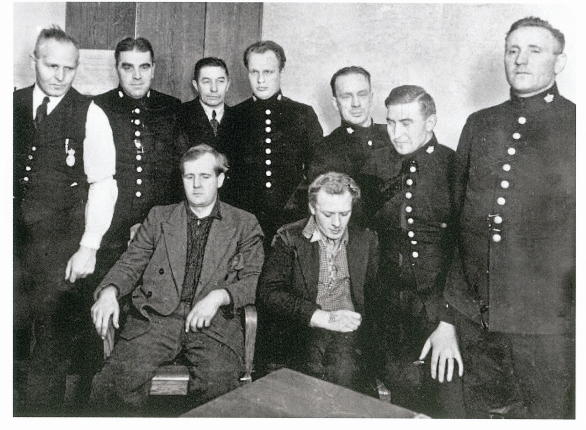 Äldre svartvitt foto av grupp män, flera bär uniformsliknande kläder