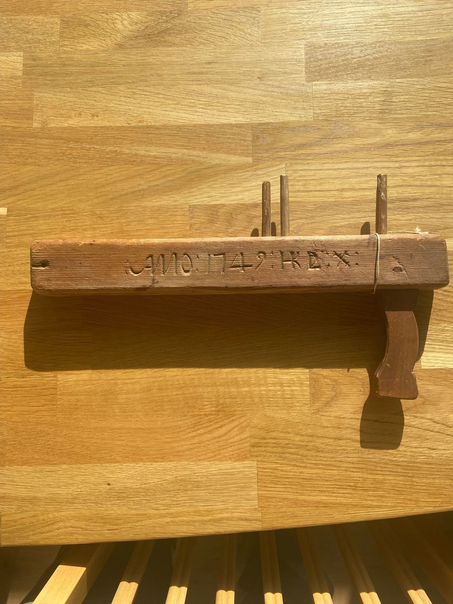 Gammalt träföremål med inskuret årtal på en ljus träyta