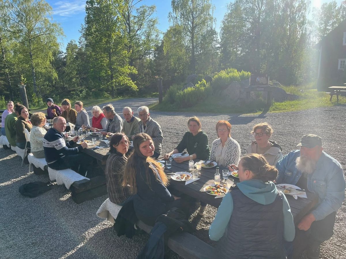 Stor grupp människor äter tillsammans vid långbord utomhus i solsken