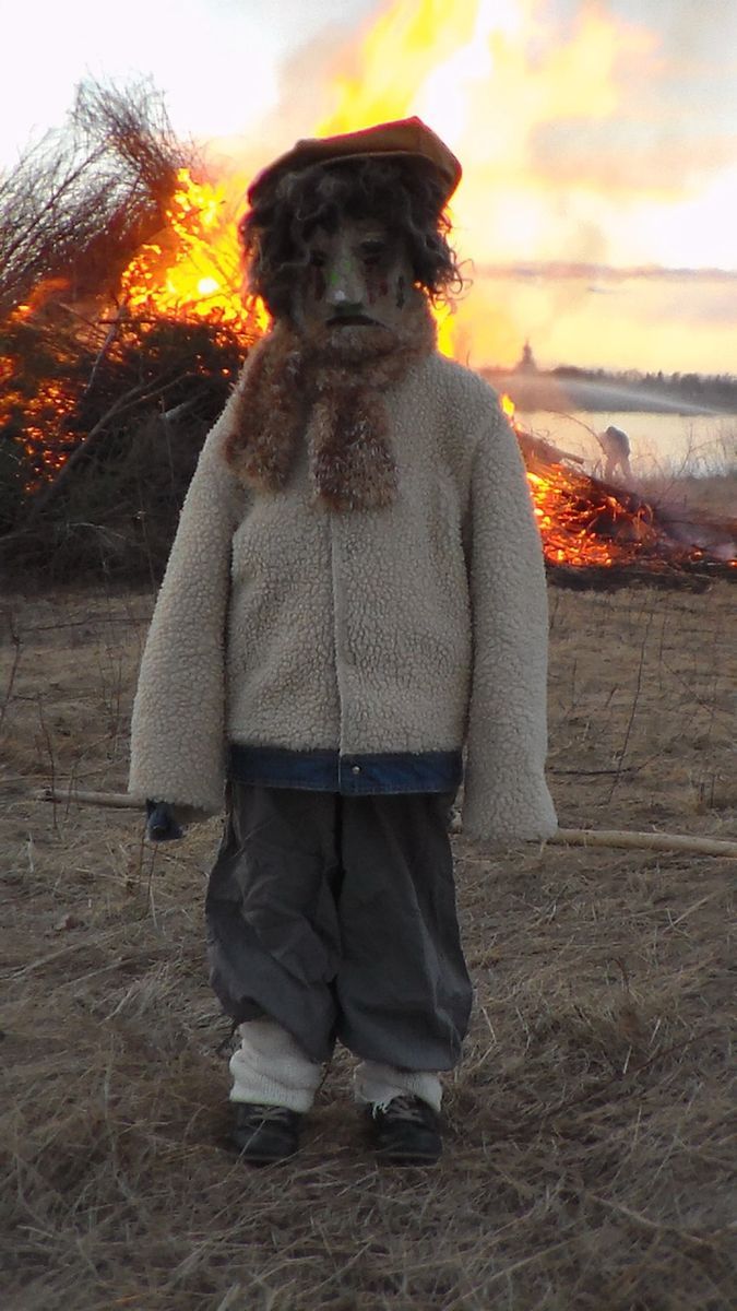 Klädd halmdocka, en valborre står på åker med majbrasa i bakgrunden.