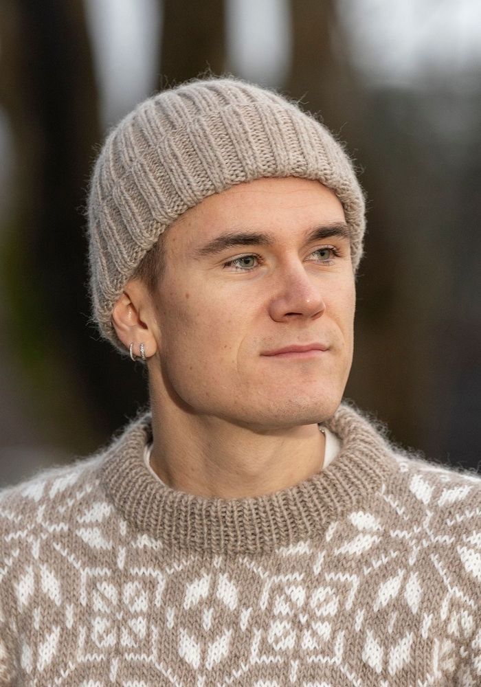 Vuxen man med stickad mössa och mönstrad tröja tittar åt sidan utomhus