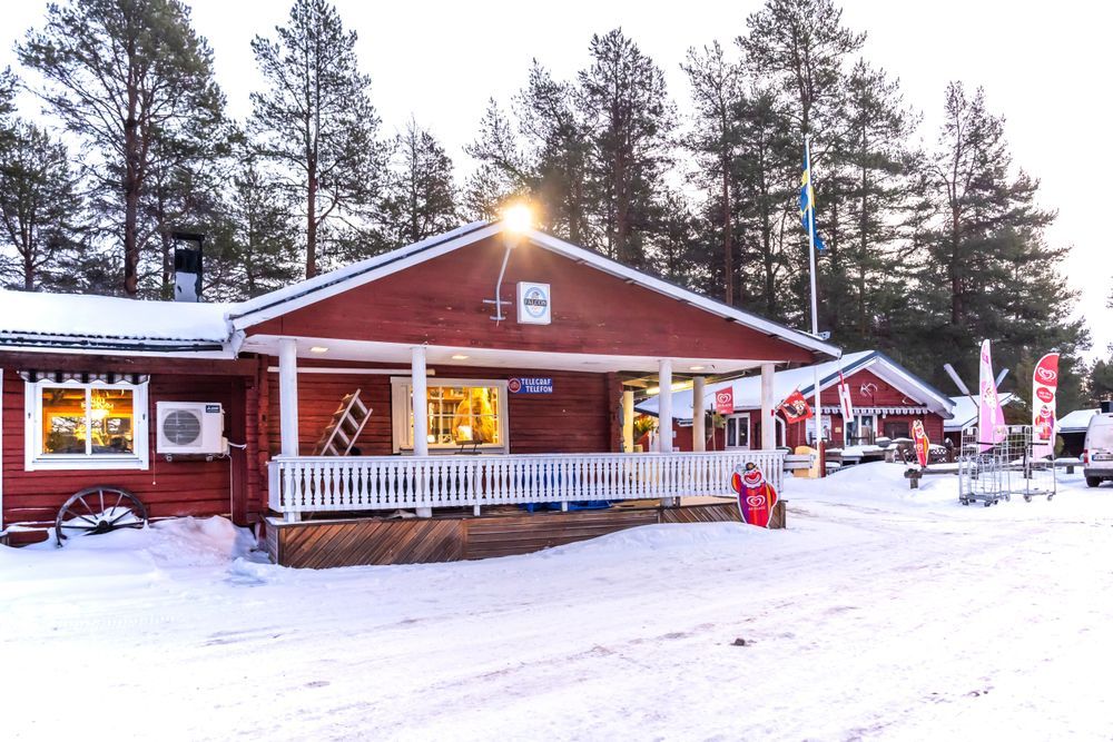 Röd byggnad med veranda, omgiven av snö och träd.