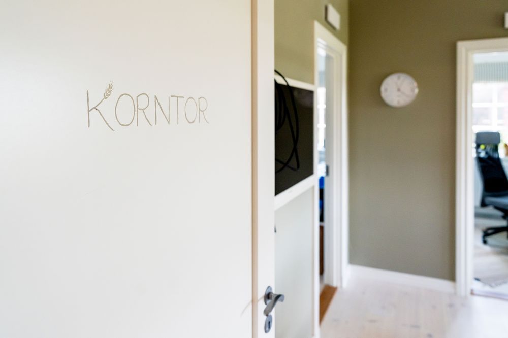 Öppen vit dörr märkt KORNTOR leder in till en ljus kontorskorridor