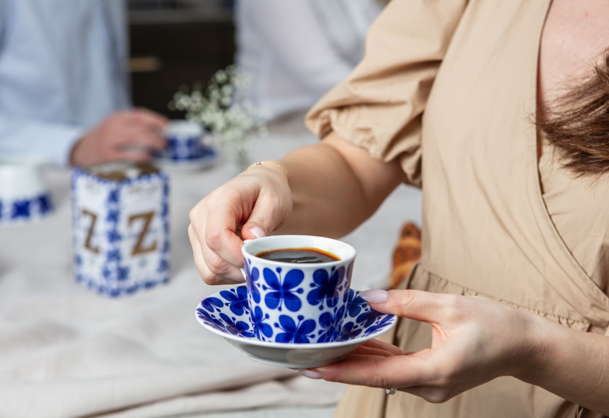 Person håller en blåvit kaffekopp vid ett dukat bord med andra i bakgrunden