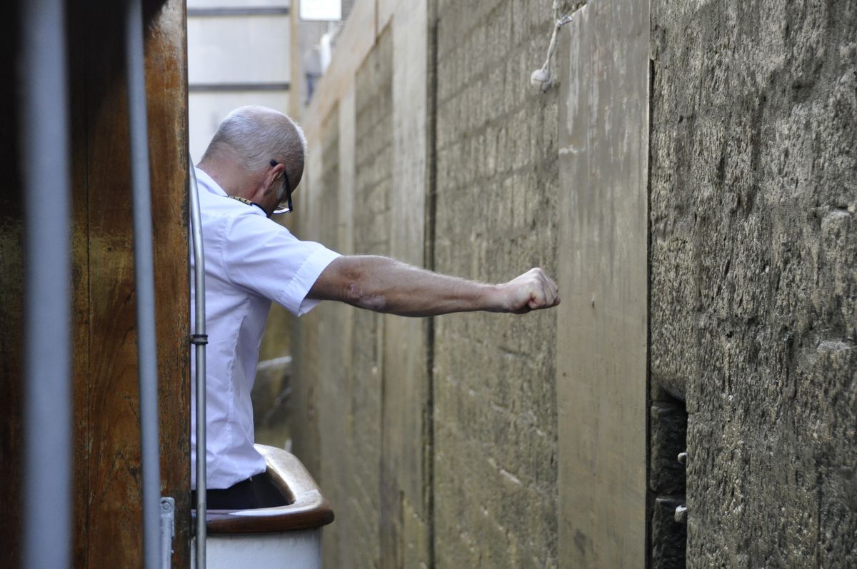Man på båt i trång passage sträcker ut armen mot murad vägg på Göta kanal-resa