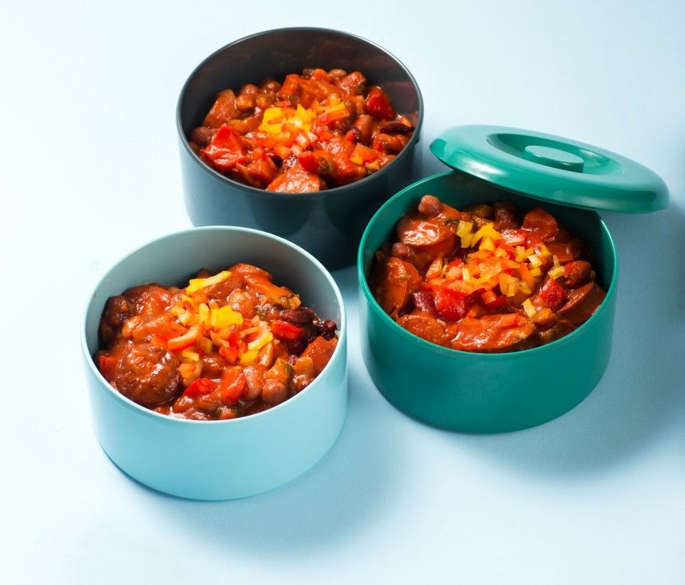 Tre matlådor med korvgryta toppad med paprika på ljus bakgrund