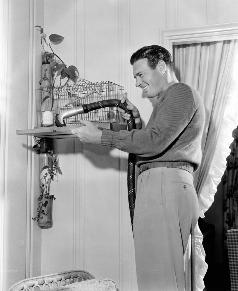 Svartvit bild på man som rengör fågelbur.