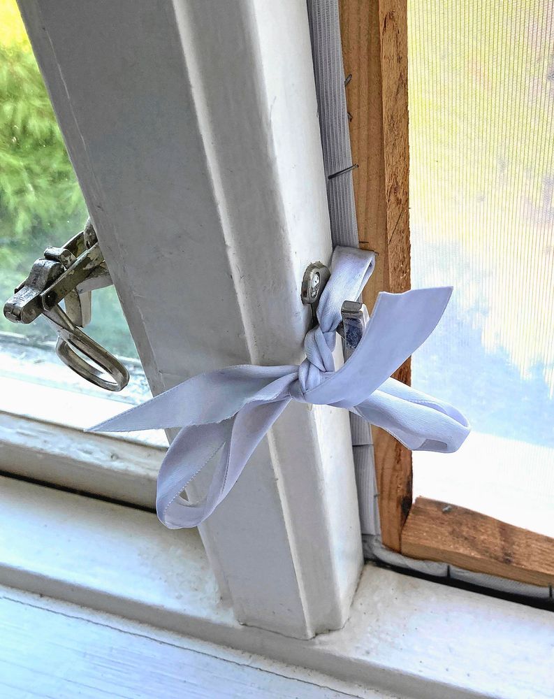 Närbild på myggfönster med knytband runt fönsterhaspen.