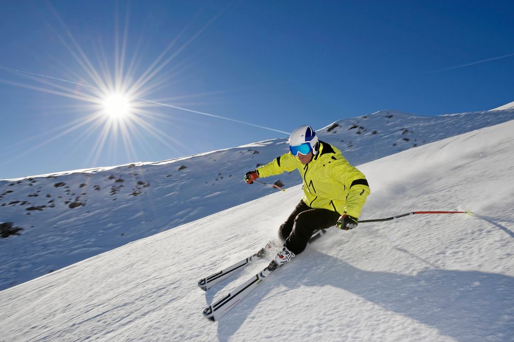 Person åker skidor nerför en solig skidbacke.
