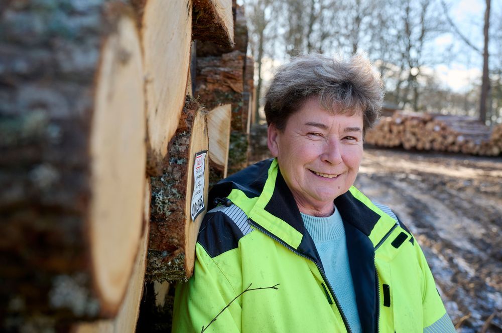 Barbara Ising i arbetskläder vid timmerstapel i skogen