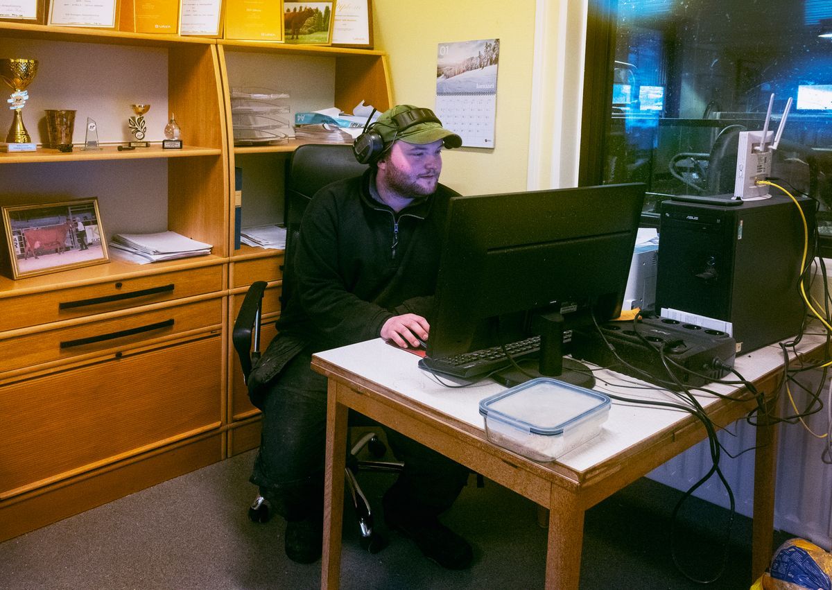 Klas vid skrivbord arbetar vid dator i enkelt kontor med hyllor och priser i bakgrunden