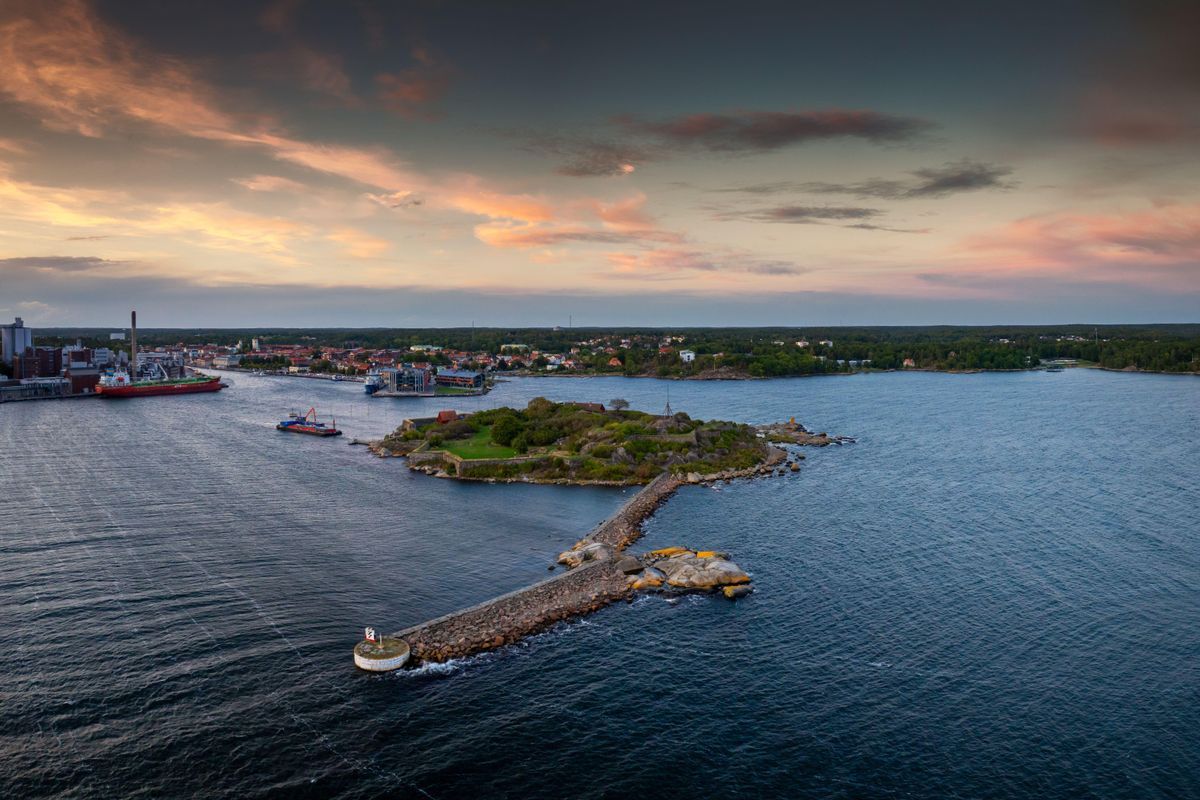 Flygvy över kuststad med hamn och grön ö vid solnedgång över havet