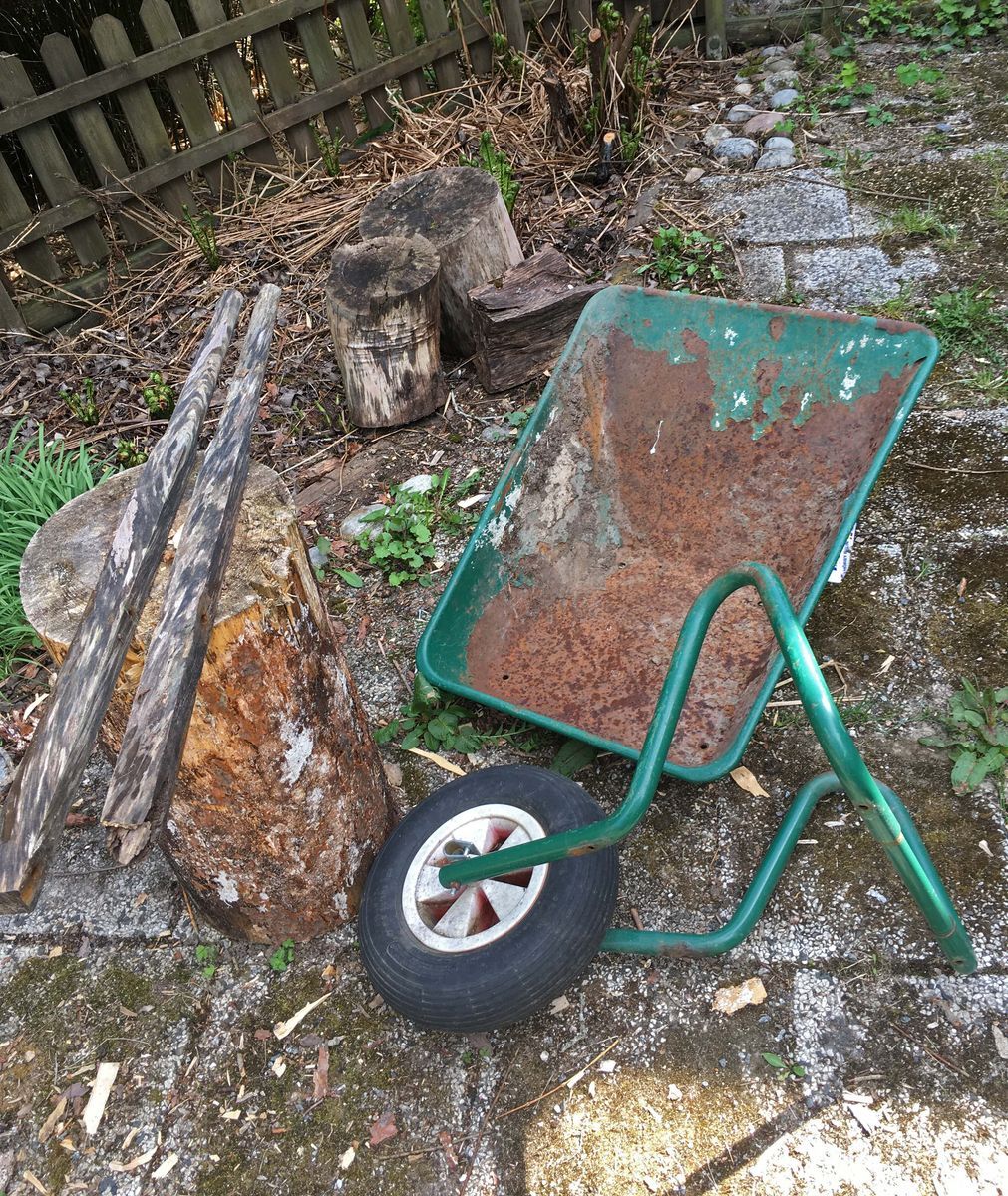Trasig, rostig skottkärra och stockar på en mossig stenlagd gård