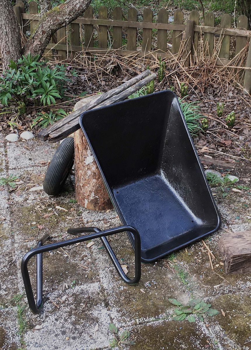 Trasig skottkärra med löst hjul och ram i en trädgård
