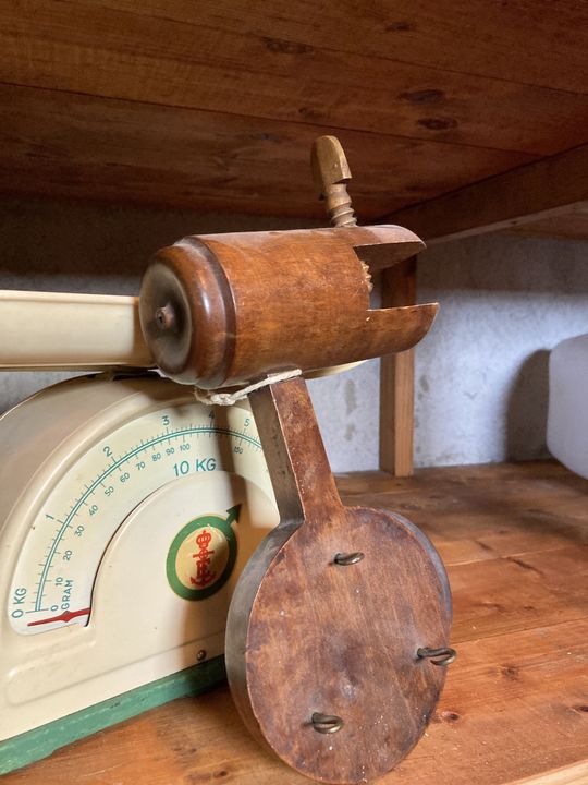 Gammaldags köksvåg i plåt med ett träredskap stående på träbord