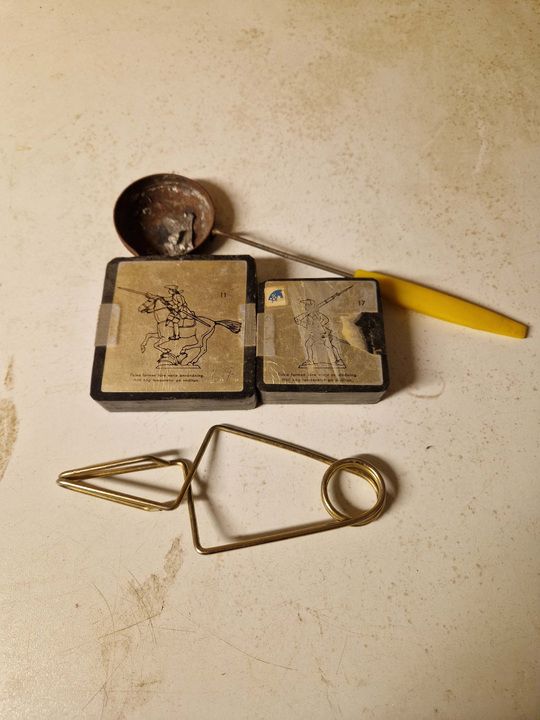 Verktyg och små graverade metallplattor liggande på ett slitet ljust bord.