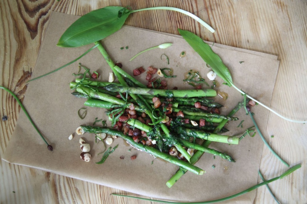 Rustik rätt med sparris, knaperstekt bacon, örter och nötter på träbord.