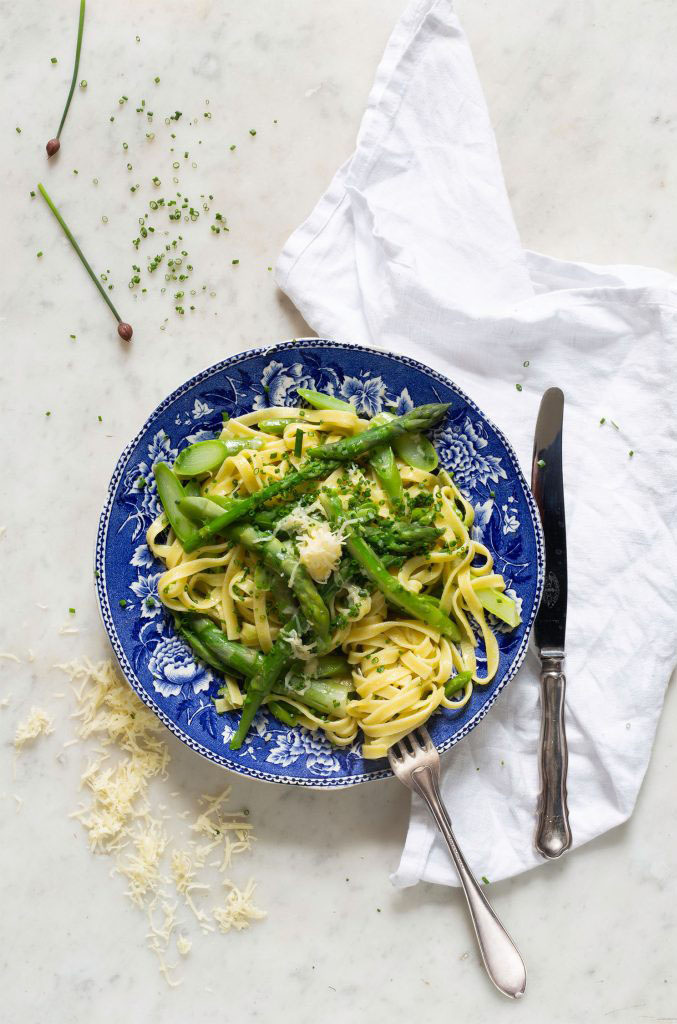 Pasta med sparris och ost serverad på blåmönstrad tallrik ovanifrån.